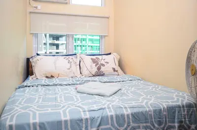 a bed with a blue and white comforter and a window at Urban Escape for You & Your Pet in Manila