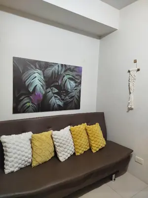 a black couch with four yellow pillows in front of a painting at Dash Shell Residences in Manila