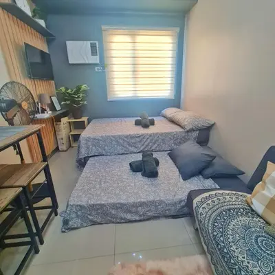 a room with three beds and a table and a window at HOMELY Green 2 Residences near DLSUHSI in Dasmariñas