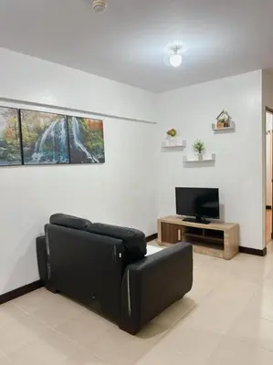 a living room with a black couch and a tv at Alea Residence 21 in Manila