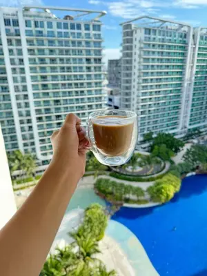 a person holding a glass of coffee in front of a city at Serene Cove Azure in Manila
