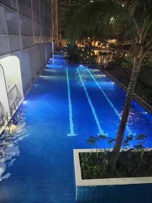 a pool at night with blue water and a palm tree at Shore residences tower D Staycation near Sm moa in Manila