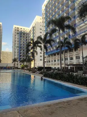 a large swimming pool with palm trees and buildings at Sea Residence Finest By Douie in Manila