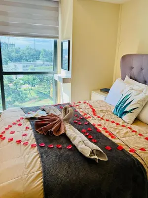 a bed with red rose petals on it with a window at Cozy Viceroy 1BR, Walk to Venice Mall in Manila