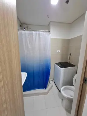 a bathroom with a toilet and a blue shower curtain at Shore 2 Residences MOA Pasay Naia in Manila