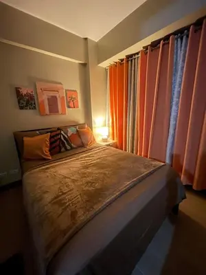 a bedroom with a large bed with orange curtains at Airport NAIA T3 Condotel in Manila