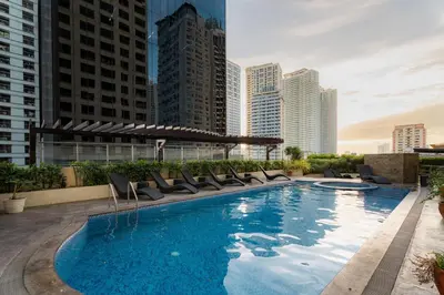 a large swimming pool with chairs and buildings at Tranquil Greenbelt Makati Condo - Free Pool Access in Manila