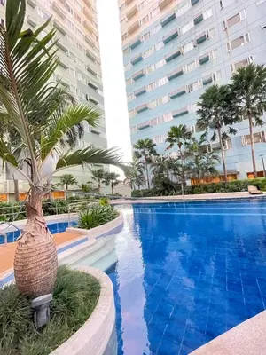 a swimming pool with a palm tree next to two tall buildings at 2BR condo unit near BGC in Manila