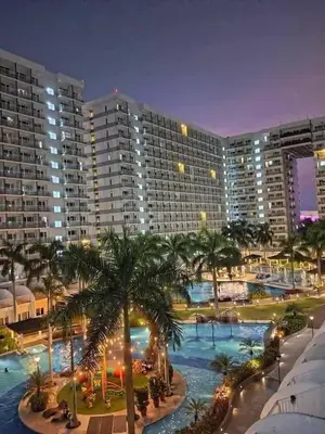 a large building with a large swimming pool with palm trees at 1BR Affordable Room infront of Mall of Asia Near Airport in Manila