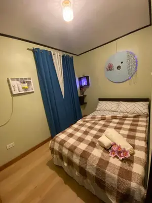 a bedroom with a bed with blue curtains and flowers on it at Casa Amaya RNR Transient House in Tanza
