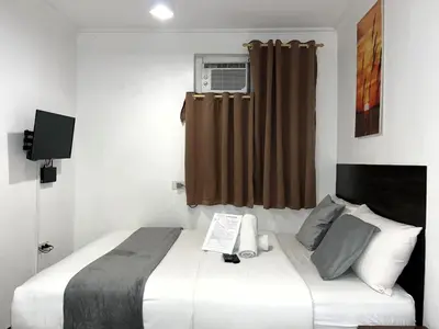 a bedroom with a bed and a window with a air conditioner at Harrison Suites in Manila