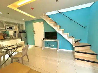 a living room with a staircase and a table and a kitchen at Cozy 2BR in BGC Fort Victoria in Manila