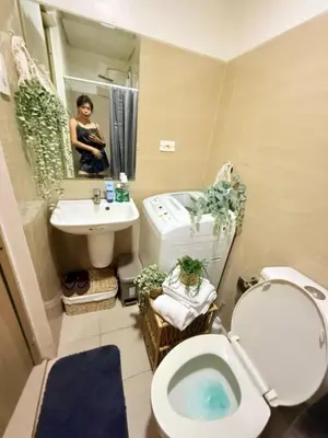 a woman taking a picture of a bathroom with a toilet and sink at City View Facing Moa in Manila