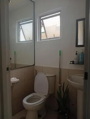 a bathroom with a toilet and a sink and two windows at Nikki's cozy home makati in Manila