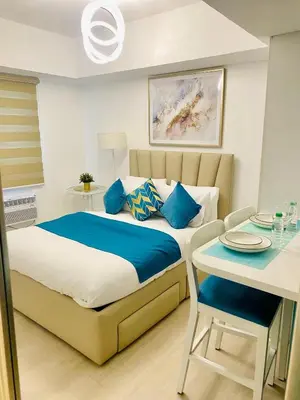 a bedroom with a bed with blue pillows and a table at SM Bicutan Condo by Santorini in Manila