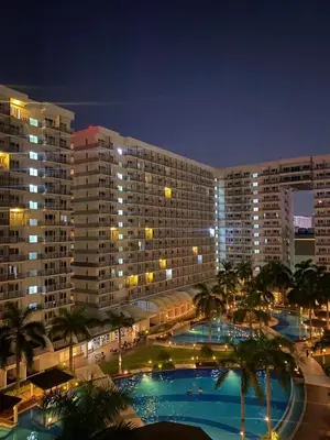 a large building with two pools and palm trees at night at Fika Staycation in Manila