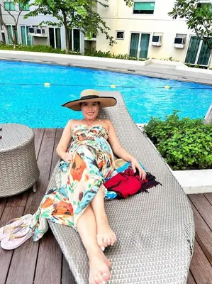 a woman in a hat sitting on a chair by a pool at Phebs 2bedroom with pool view in the heart of Makati in Manila
