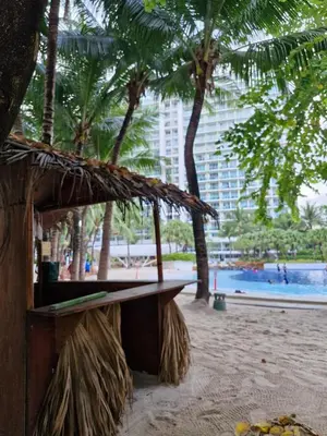 a bench on a beach with palm trees and a building at Hiraya Pod Staycation Netflix Balcony Beach Escape in Manila