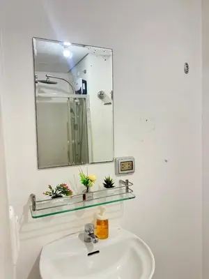a white bathroom with a sink and a mirror at Cozy Nook in the City of Mandaluyong in Manila