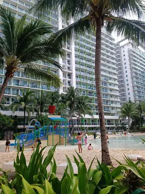 a beach with a playground and palm trees and buildings at Azure Urban Resort Staycation in Manila