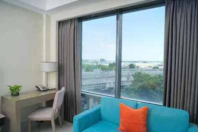 a room with a blue couch and a desk and a large window at Stay Across NAIA Terminal 3 in Newport City in Manila