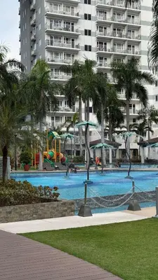 a large swimming pool with palm trees and a building at Spacious Condo at Shell Residences, MOA Pasay - The Urban Stay in Manila
