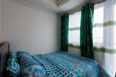 a bed in a room with two windows at Fully Furnished 1BR Condo at Jazz Residences in Manila