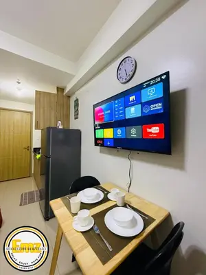 a dining room table with plates and a tv on a wall at EMZ SHORE2 Staycation 16 in Manila