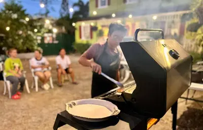 a man cooking food on a grill with a pan at Madie's Place B&B with Private Pool in Santa Rosa near Enchanted Kingdom in Santa Rosa