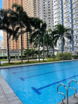 a large swimming pool with palm trees and buildings at Light Residence Condo with Pool View in Manila