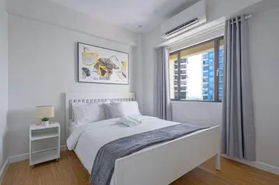 a white bedroom with a bed and a window at 1 BR Central and Cozy Condo Prime Location in BGC in Manila