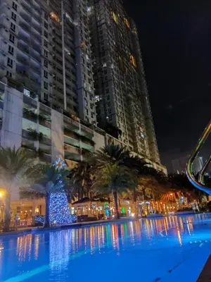 a large swimming pool with palm trees in front of buildings at Condo in Pasay 12th flr studio unit-near MOA, PICC in Manila