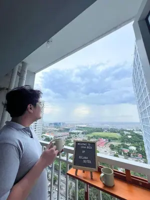 a woman holding a cup of coffee looking out of a window at Bay View near US Embassy, Airport in Manila
