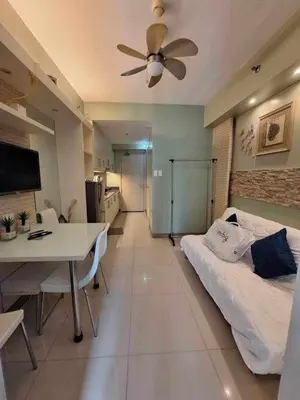 a room with a bed and a table and a ceiling fan at Sea Residences MOA Oasis-Nicolai Ramos in Manila