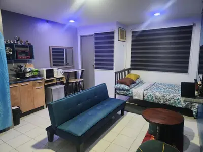 a bedroom with a blue couch and a kitchen at El Cozy Woody Near Enchanted Kingdom in Santa Rosa