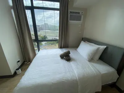 a teddy bear sitting on a bed with a window at 2-min Walk to Okada Near AirportMOA wBalcony in Manila