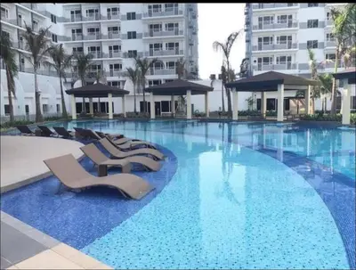 a large swimming pool with lounge chairs and a building at Relax in Pasay City at Shell Residences - Your Home Away from Home in Manila