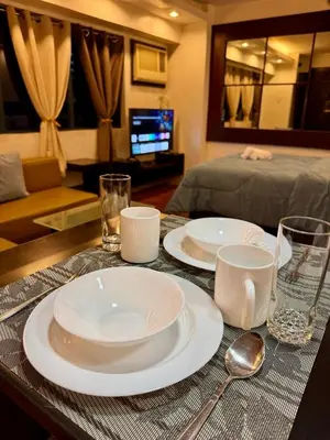a table with two white plates and glasses on it at WestParc Cedar Cozy Apartment in the Heart of Alabang in Manila