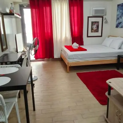 a bedroom with a bed with red curtains and a desk at Cozy Gutz Place at 16th in Manila
