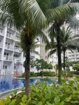 a hotel with palm trees in front of a swimming pool at staycation condo one bedroom balcony w pool view near SMX SM MOA IKEA NAIA DFA OCEAN PARK in Manila