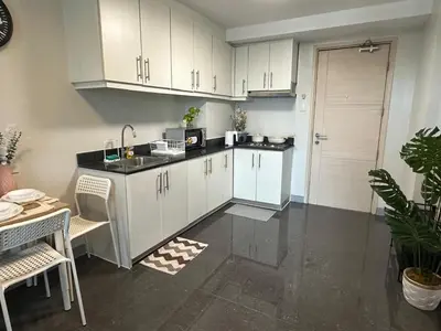 a kitchen with white cabinets and a sink and a table at Suite Haven - Sea Residences MOA PASAY in Manila