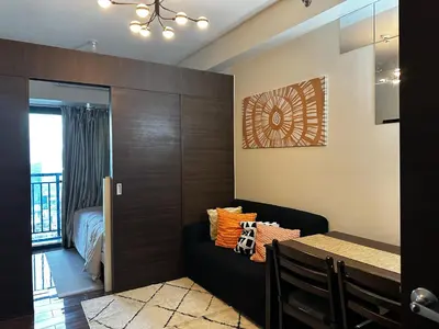 a dining room with a black couch and a bedroom at MySunset at Air Residences Makati in Manila