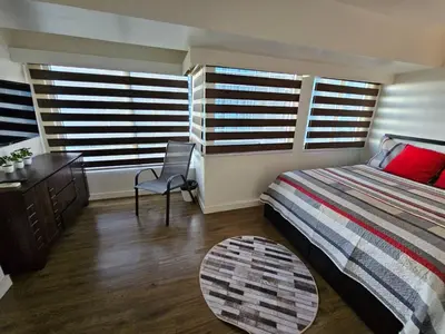 a bedroom with a bed and a desk and two windows at Casa Rosa3 2BR loft in BGC 5 people in Manila