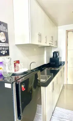 a kitchen with white cabinets and a black dishwasher at Yoona era Staycation in Manila