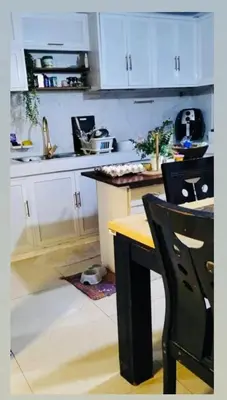 a kitchen with white cabinets and a table and a chair at Vacation Home by Rowena Sacarez in Trece Martires