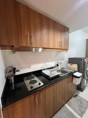 a kitchen with wooden cabinets and a black counter top at Calle Homes - 1BR unit with balcony, LUSH RESIDENCES in Manila