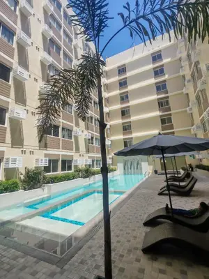 a palm tree and an umbrella next to a swimming pool at Family-Friendly 2BR Staycation near Nuvali & Enchanted Kingdom in Puting Kahoy