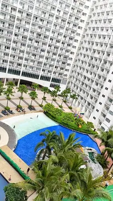 a large apartment complex with a large swimming pool with palm trees at Pool view from one-bedroom condo at Shore Residence in Manila