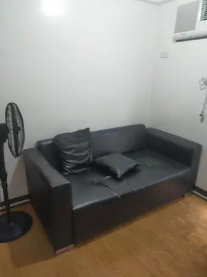 a black leather couch in a room with a fan at May homey vibe in Pasig