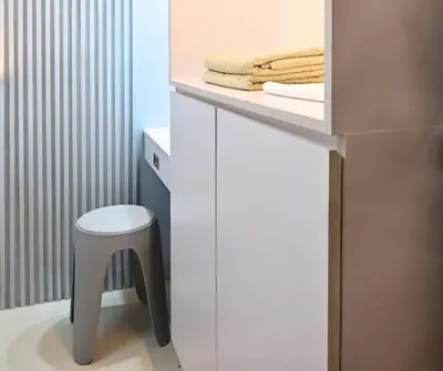 a bathroom with a white vanity with a stool and towels at Chic & Cozy Urban Stay in Manila
